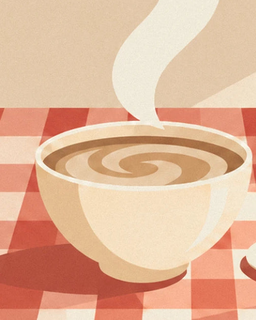 The large bowl of steaming milky coffee on the red checked tablecloth