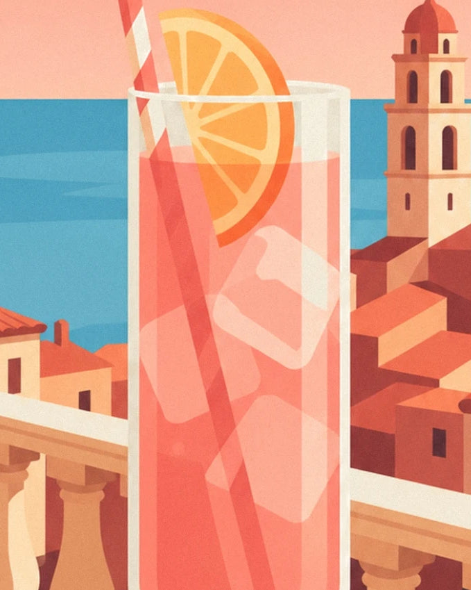 Un cocktail rosé avec glaçons, paille rayée et tranche d’orange face à la mer