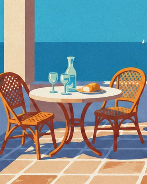 La table ronde avec carafe, 2 verres et pain, entre 2 chaises en rotin face à la mer